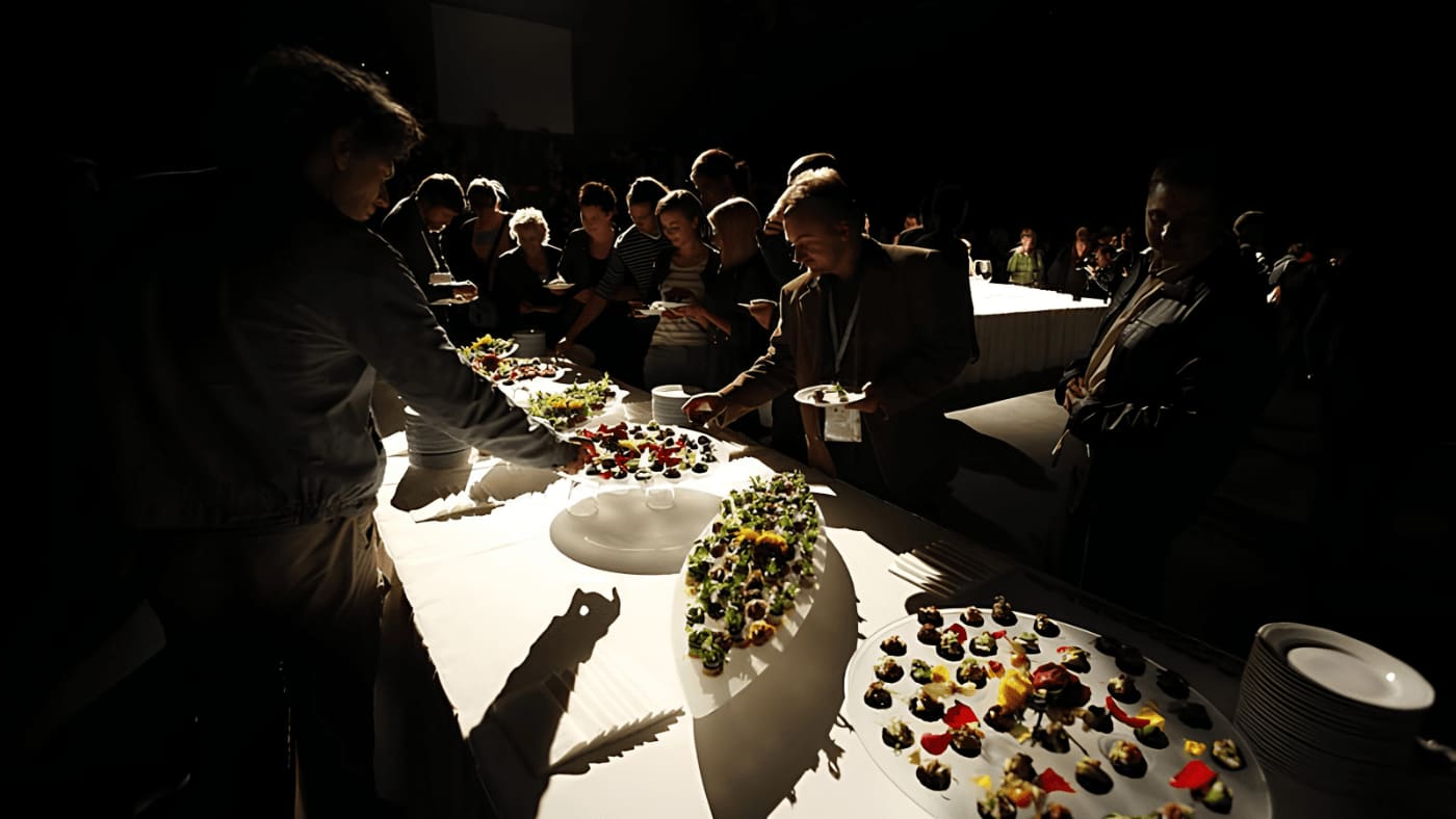 Audience members gathered in a dark performance space around a brightly lit table of edible sensory works at the European Congress of Culture.